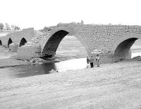 Tres personas contemplan los ojos del puente de Villanueva del Río. / NURIA ESTALAYO/